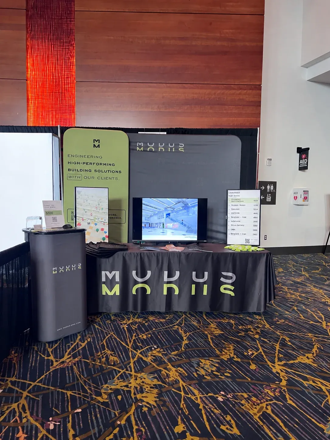 MODUS Road at the MODUS booth at AIA Iowa: a portrait game display, the project work screen and the leaderboard monitor