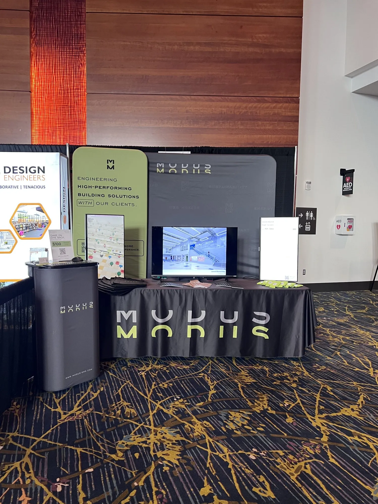 The MODUS booth at AIA Iowa from the front, with screens, signs and the MODUS table