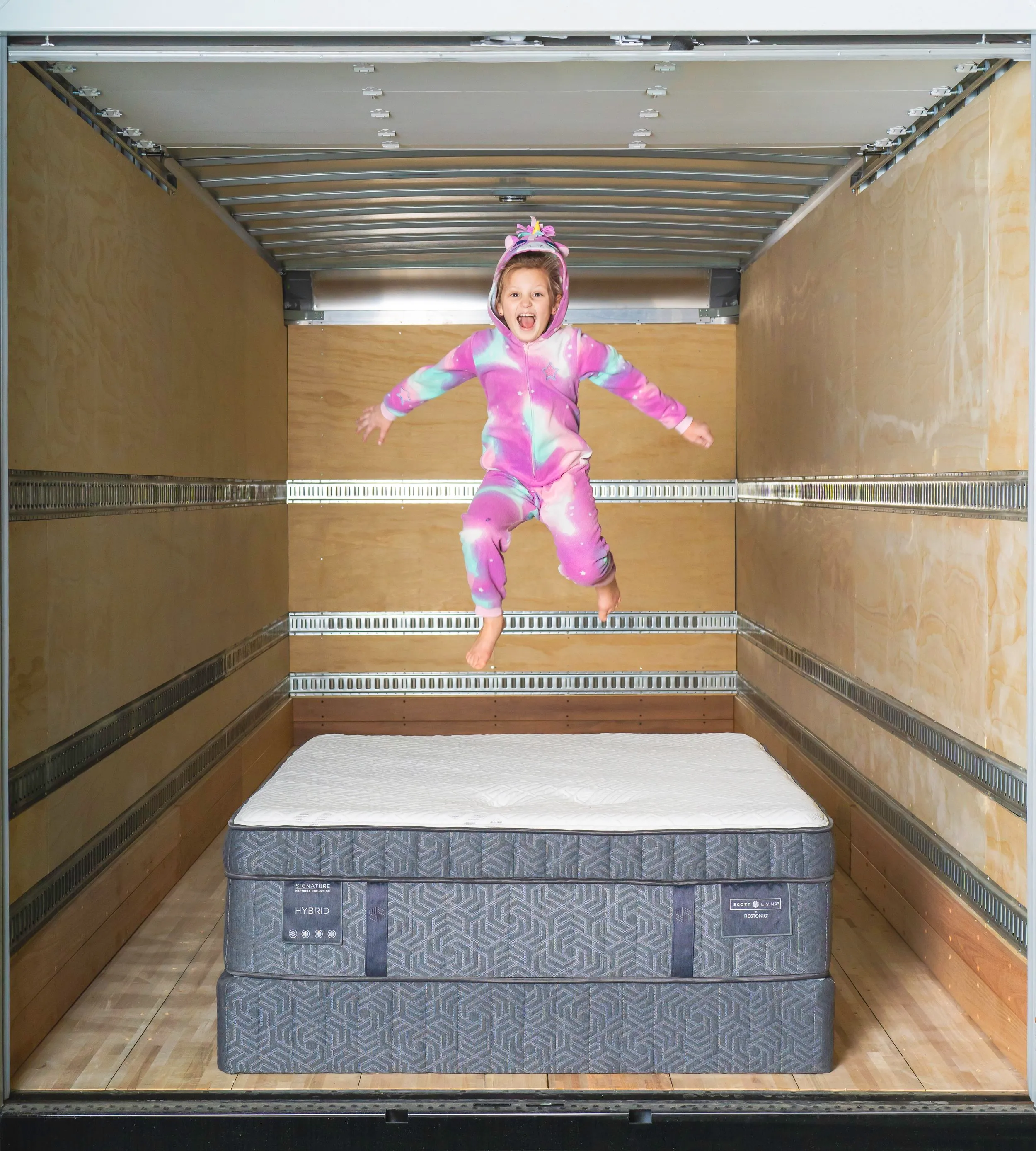 Child jumping on a mattress in the back of a Midwest Mattress delivery truck